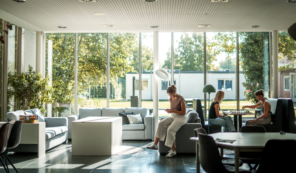 Twee personen zijn aan het schaken en er zit een ander persoon bij hen in de kantine.