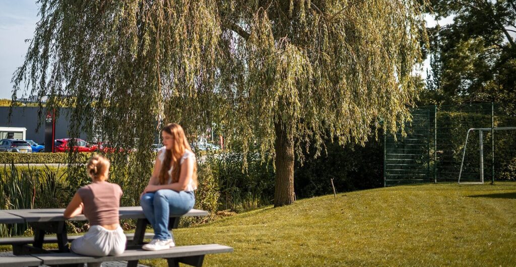 Twee personen zitten in de zon in de tuin van College Campus Meppel.